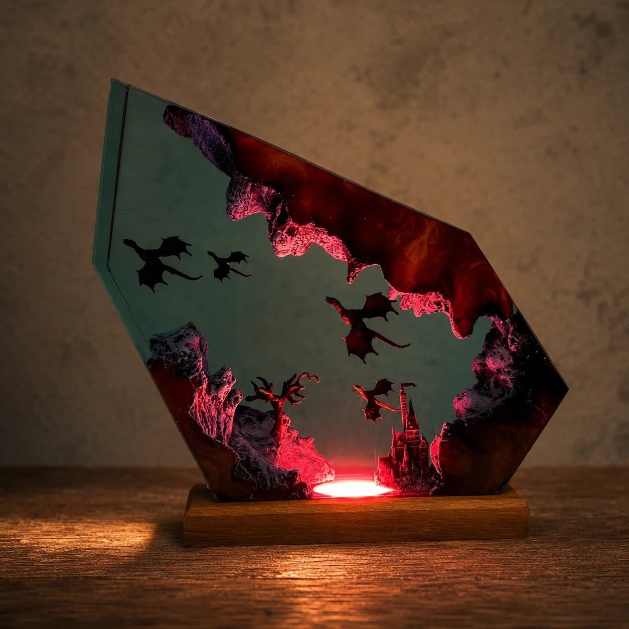 A fantasy-themed LED light shaped like a jagged crystal, featuring silhouettes of dragons and a castle against a teal sky, illuminated with a warm red glow from a wooden base on a wooden table.