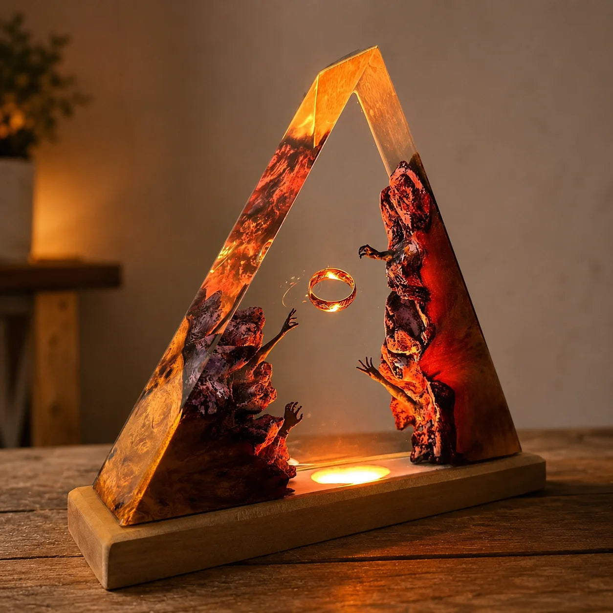 A triangular resin lamp or decorative sculpture on a wooden base, lit from within with warm amber and orange glow. The resin features swirling red, orange, and dark brown marbled patterns, with a small floating ring in the center.
