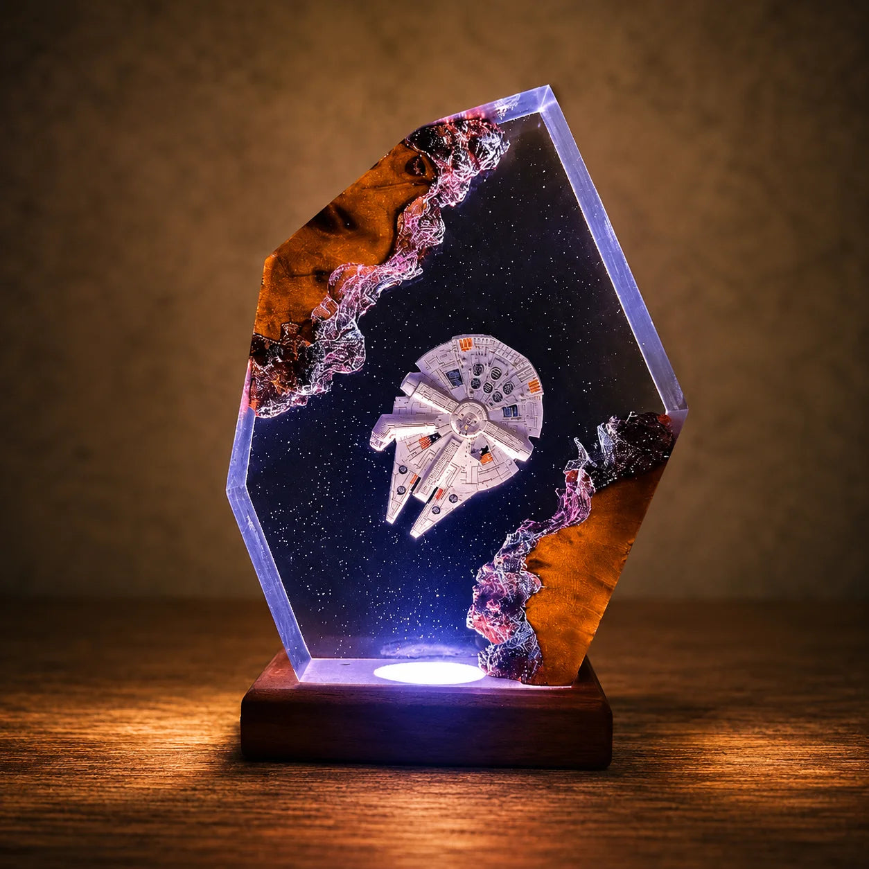 A decorative acrylic resin plaque featuring a miniature Millennium Falcon model inside a starry black background, mounted on a dark wooden base that glows with blue light. The plaque has natural brown and purple crystalline inclusions, set on a wooden surface against a warm, textured brown background.