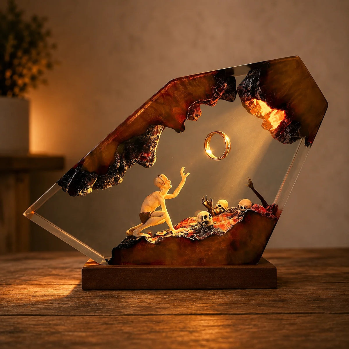 A decorative resin display sculpture on a wooden base, featuring a small kneeling human figure reaching toward a floating ring, with skulls and dark textured organic forms inside a clear geometric frame. The piece is photographed on a tabletop in a warmly lit indoor setting.