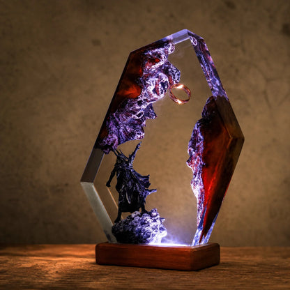 A hexagonal resin lamp featuring a dark fantasy scene with a black silhouette figure, purple rocky formations, and a gold ring, illuminated from within on a wooden base.