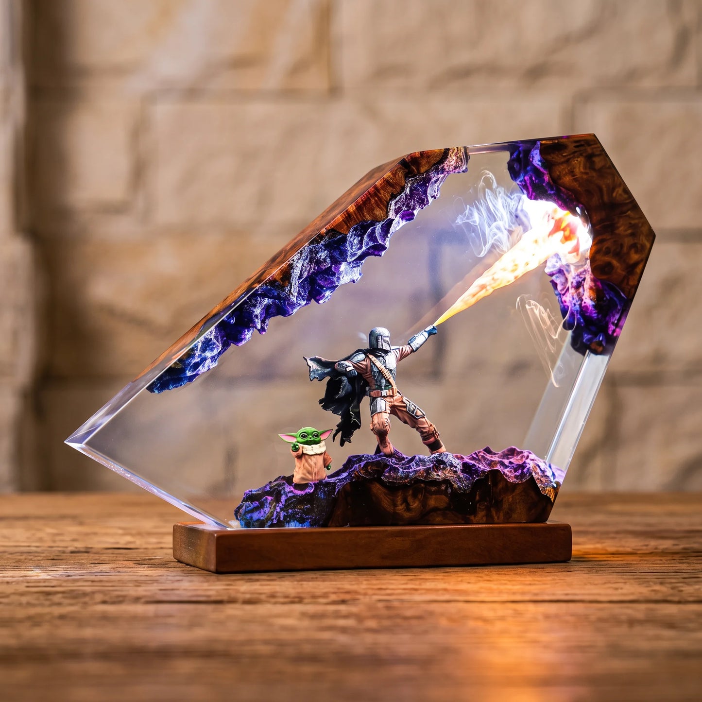 A clear acrylic diorama display on a wooden base, featuring a small figurine of a warrior shooting a flame-like projectile, with purple rock formations and a small green character inside. The acrylic is shown on a wooden table with a blurred stone wall background.